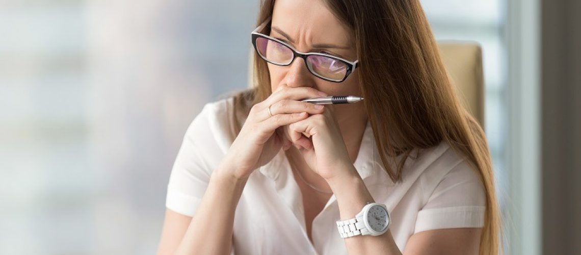 Worried businesswoman sitting alone in office. Pensive middle-aged woman resting her head on hands and looks aside in window. Concentrated female entrepreneur frowning thinking about problem solution